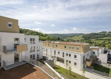 Moderne Wohnanlage mit weißer Fassade, Balkonen und weitem Blick ins Grüne.