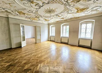 Großzügiger Raum mit beeindruckender Stuckdecke, Fischgrätparkett und hohen Fenstern, ideal als Wohnzimmer.