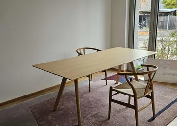 Heller Essbereich mit modernem Holztisch und Stühlen, große Fenster bieten Blick ins Grüne.