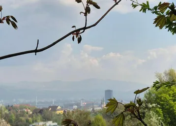 Panoramablick über eine grüne Hügellandschaft mit einer Stadt und Bergen im Hintergrund.