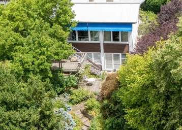 Luftaufnahme eines Hauses mit weitläufigem Garten und blauer Markise, umgeben von üppigem Grün.