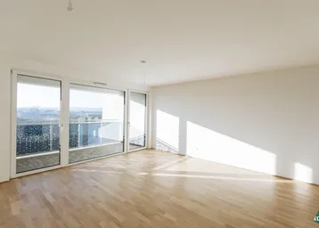 Helles Wohnzimmer mit Parkettboden, großen Fenstern und Zugang zu einem Balkon.