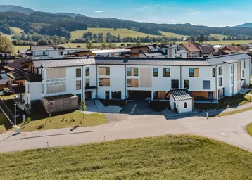 Moderne Neubau-Wohnanlage mit weißer Fassade und Holzakzenten in einer grünen, ländlichen Umgebung.