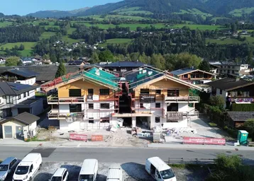 Luftaufnahme von Neubauten in Holzbauweise, eingebettet in eine grüne Berglandschaft.