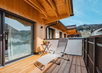 Sonniger Balkon mit Holzfußboden, Liegestuhl und weitem Blick auf die umliegende Landschaft.