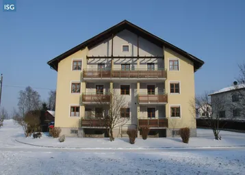 Mehrfamilienhaus mit mehreren Balkonen und Satteldach in verschneiter ländlicher Umgebung.