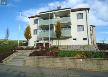 Modernes Mehrfamilienhaus mit Balkonen und gepflegter Außenanlage unter blauem Himmel.