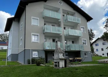 Mehrfamilienhaus mit modernen Glasbalkonen, umgeben von Grünflächen und einem Außenkamin.