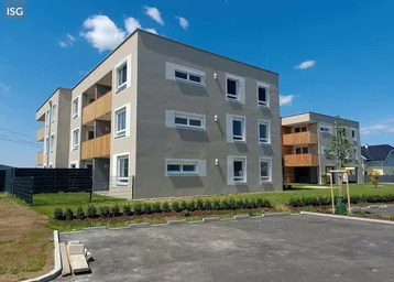 Moderne Wohngebäude mit Balkonen und gepflegter Außenanlage unter blauem Himmel.