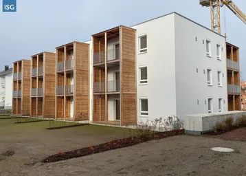 Moderne Wohngebäude mit Holzfassaden und Balkonen, umgeben von einer noch unfertigen Grünfläche.