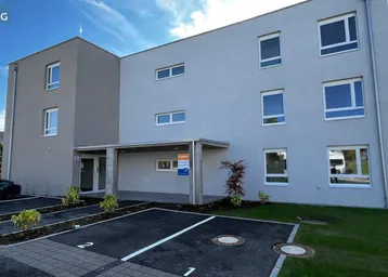 Modernes Mehrfamilienhaus mit heller Fassade, großen Fenstern und Parkplätzen im Freien.