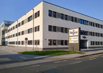 Modernes Bürogebäude mit weißer Fassade und großen Fenstern, gelegen an einer Straße.
