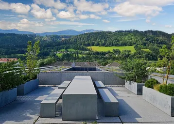 Große Dachterrasse mit modernen Betonmöbeln und weitem Blick auf bewaldete Berge und den Himmel.