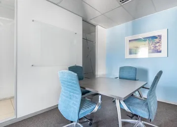 Modernes Besprechungszimmer mit blau gepolsterten Stühlen, einem grauen Tisch und einer Whiteboard-Wand für Notizen.