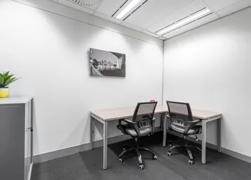 Kleines, modernes Büro mit zwei Arbeitsplätzen, weiß gestrichenen Wänden und grauem Teppichboden.