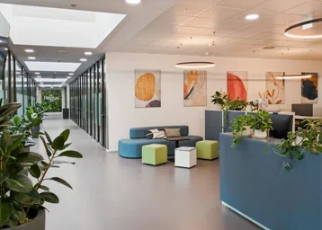 Moderner Bürobereich mit Lounge-Sitzgelegenheiten, Pflanzen und einem langen Flur mit Glaswänden.