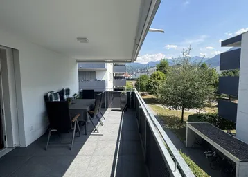 Geräumiger Balkon mit Fliesenboden und Sitzgelegenheiten, umgeben von Grün und Bergblick.