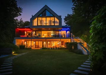 Moderne Villa bei Nacht mit beleuchteten Terrassen und großzügiger Gartenanlage am Seeufer.