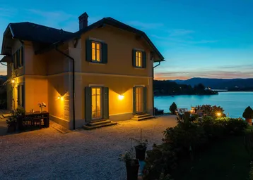 Elegantes Haus am Seeufer bei Sonnenuntergang mit beleuchteter Fassade und Seeblick.