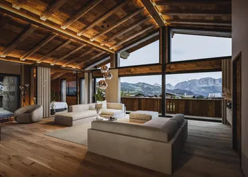 Geräumiges Wohnzimmer mit Holzbalkendecke, großen Fenstern und atemberaubendem Bergblick.