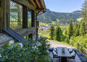 Große Holzterrasse mit Esstisch und Stühlen, umgeben von alpiner Natur und Bergblick.