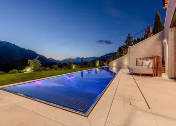 Langer, beleuchteter Pool mit atemberaubendem Bergblick und Liegebereich am Abend.