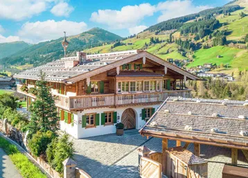 Traditionelles Alpenchalet mit Holzbalkonen und grünen Fensterläden, eingebettet in eine malerische Berglandschaft.
