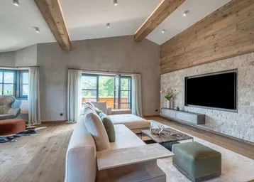 Geräumiges Wohnzimmer im alpinen Stil mit Holzbalken, Steinwand und Zugang zum Balkon.