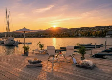 Holzterrasse am See mit Sitzgelegenheiten und Blick auf den Sonnenuntergang über den Bergen.