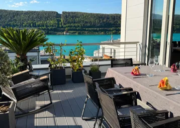 Geräumige Terrasse mit Esstisch, Pflanzen und herrlichem Blick auf den See und die Berge.