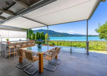 Große überdachte Terrasse mit Esstisch, Außenküche und atemberaubendem Blick auf den See und die Berge.