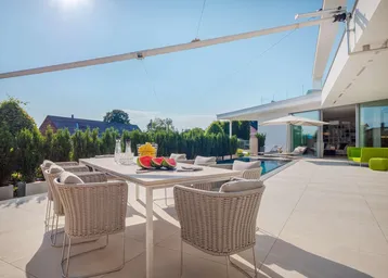 Moderne Terrasse mit Esstisch, Korbstühlen und Blick auf den Pool und die umliegende Landschaft.