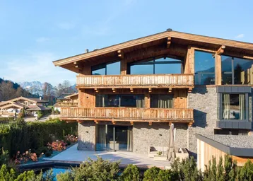 Traditionelles Chalet mit Holzfassade, Steinmauern und Bergblick unter blauem Himmel.