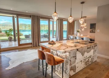 Luxuriöse offene Küche mit Marmorinsel und Essbereich, mit direktem Zugang zur Terrasse und Seeblick.
