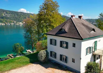 Elegantes Haus mit weißer Fassade und grünem Dach, direkt am See mit Bergblick gelegen.