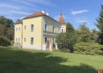 Historisches Gebäude mit gelber Fassade und rotem Ziegeldach, umgeben von einem weitläufigen Garten.