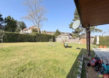 Gartenbereich mit hoher Hecke, Bäumen und Kinderspielgeräten.