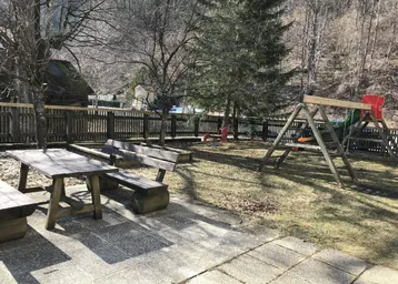 Großer Gartenbereich mit Spielplatz, Sandkasten und Sitzgelegenheiten, umgeben von Natur und Bergen.