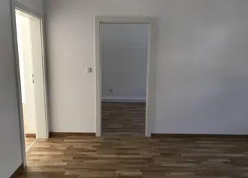 Leerer Raum mit hellem Parkettboden und zwei offenen Türrahmen, bereit zum Einzug.