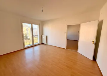 Helles Zimmer mit Laminatboden, weiß gestrichenen Wänden und Zugang zu einem kleinen Balkon.