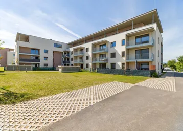 Modernes Mehrfamilienhaus mit mehreren Balkonen und gepflegter Grünfläche in sonniger Umgebung.