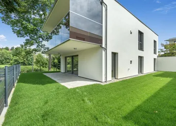 Moderne Architektur mit weißer Fassade, großen Glasflächen und gepflegtem Rasenbereich mit Terrasse.