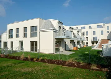 Moderne Wohnanlage mit weißer Fassade, Balkonen und gepflegter Rasenfläche unter blauem Himmel.
