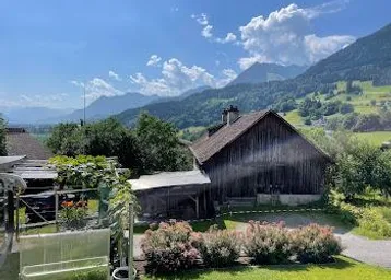Idyllischer Gartenbereich mit traditioneller Scheune und weitem Blick auf die umliegende Berglandschaft.