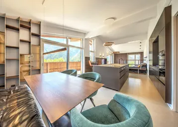 Heller, offener Wohn- und Essbereich mit moderner Küche, Bergblick und Zugang zum Balkon.