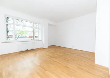 Helles, leeres Zimmer mit Parkettboden und großem Fenster, bereit zur individuellen Gestaltung.