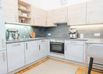 Moderne Küche mit hellen Holzschränken, grauen Arbeitsplatten und Holzboden.