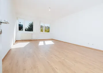 Helles, leeres Zimmer mit Laminatboden und zwei Fenstern, die viel Tageslicht hereinlassen.