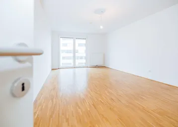 Helles, leeres Zimmer mit Parkettboden und Zugang zu einem Balkon, ideal als Wohn- oder Schlafzimmer.