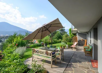 Große Terrasse mit Holzdeck, Gartenmöbeln und einem weiten Blick auf die Berge und die grüne Landschaft.